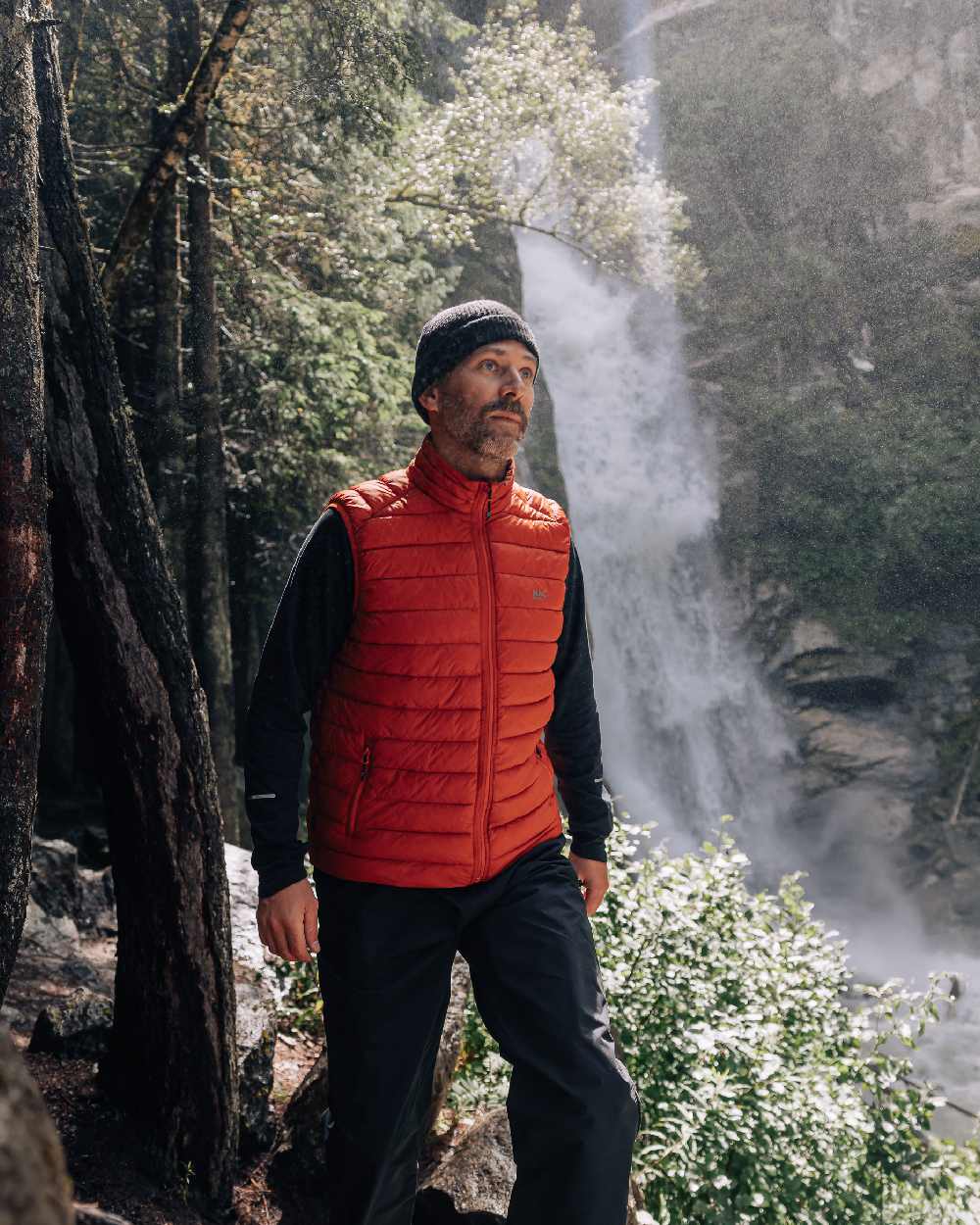Burnt Orange Coloured Mac In A Sac Mens Synergy Gilet on waterfall background 