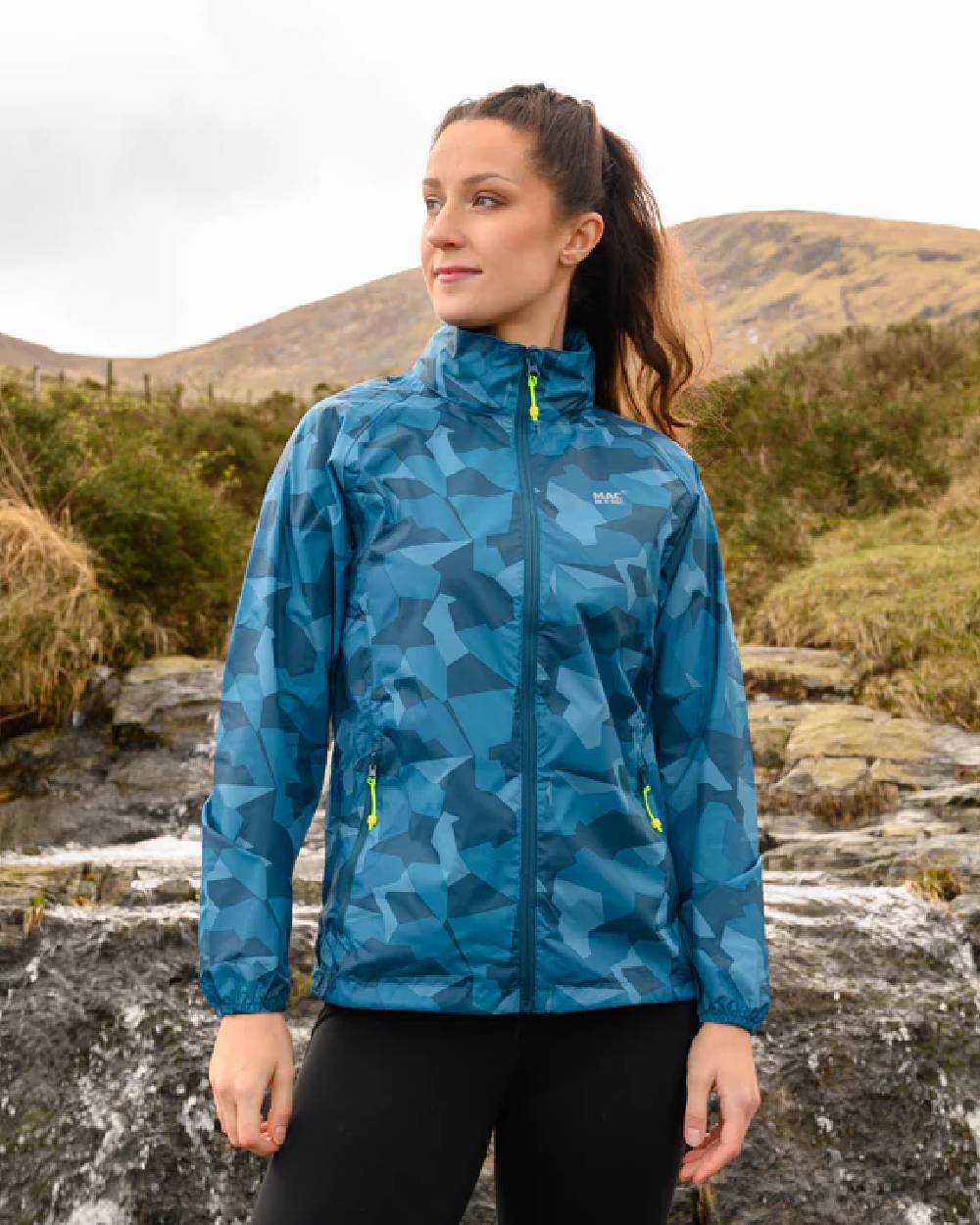 Teal Camo Coloured Mac In A Sac Origin Camo Packable Waterproof Jacket on mountain background 