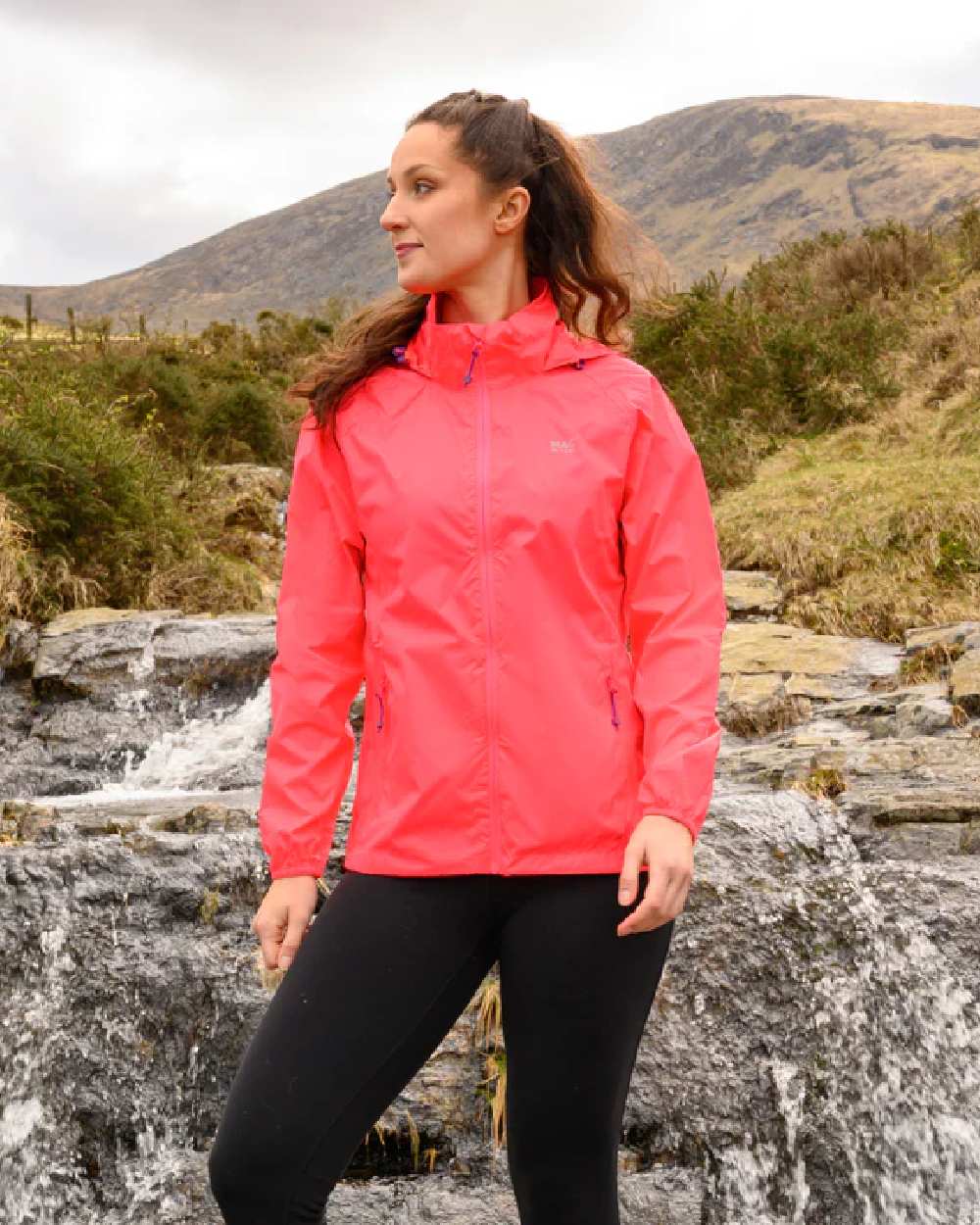 Neon Watermelon Coloured Mac In A Sac Origin Neon Packable Waterproof Jacket on blurry background 