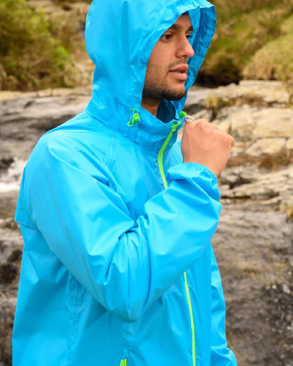 Neon Blue coloured Mac In A Sac Packable Origin Neon Waterproof Jacket on blurry mountain background 