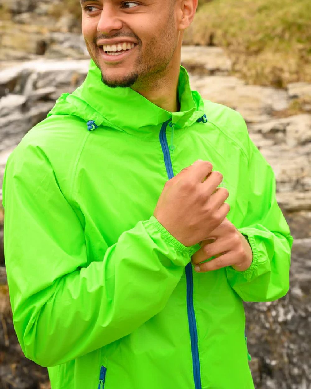 Neon Green coloured Mac In A Sac Packable Origin Neon Waterproof Jacket on blurry mountain background 