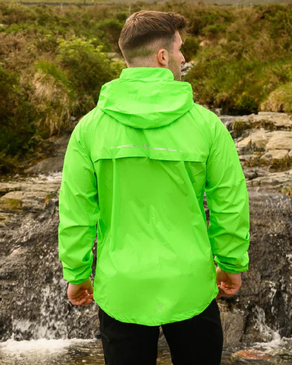 Neon Green coloured Mac In A Sac Packable Origin Neon Waterproof Jacket on blurry mountain background 