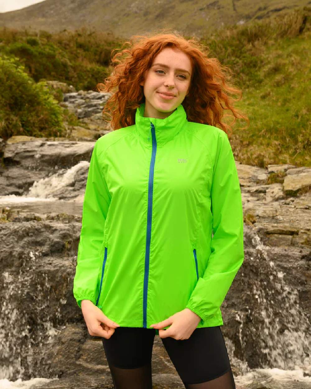 Neon Green coloured Mac In A Sac Packable Origin Neon Waterproof Jacket on blurry mountain background 