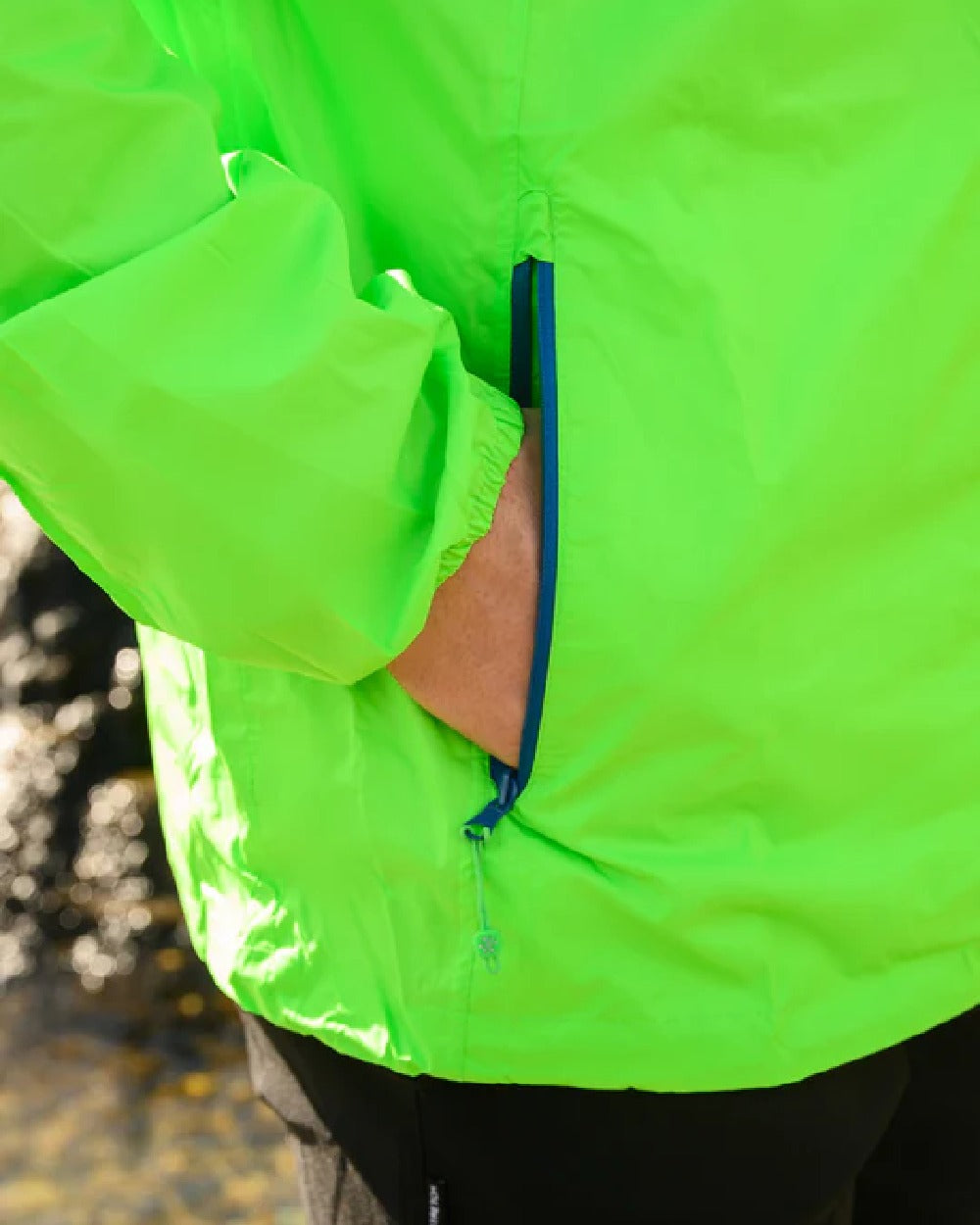 Neon Green coloured Mac In A Sac Packable Origin Neon Waterproof Jacket on blurry mountain background 