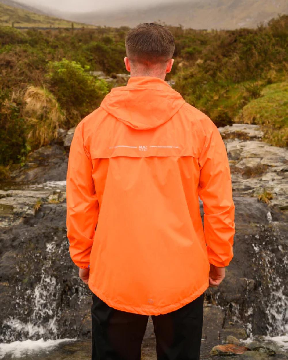 Neon Orange coloured Mac In A Sac Packable Origin Neon Waterproof Jacket on blurry mountain background 