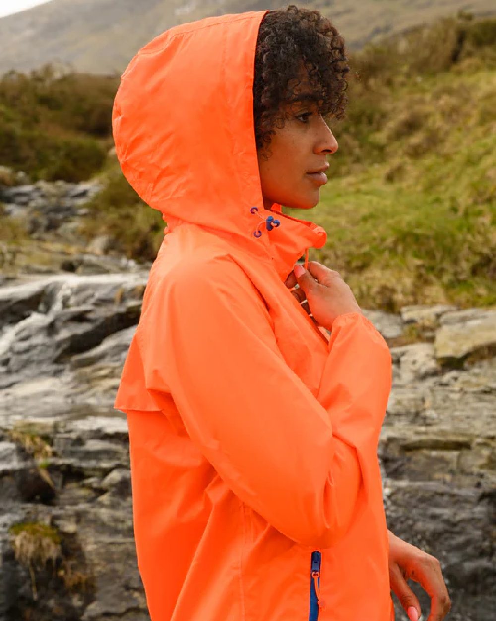 Neon Orange coloured Mac In A Sac Packable Origin Neon Waterproof Jacket on blurry mountain background 