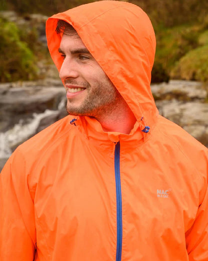 Neon Orange coloured Mac In A Sac Packable Origin Neon Waterproof Jacket on blurry mountain background 
