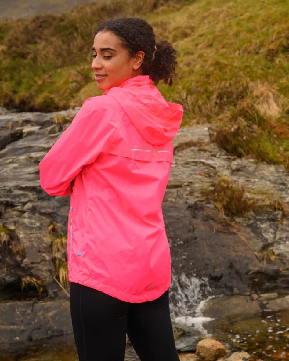 Neon Pink coloured Mac In A Sac Packable Origin Neon Waterproof Jacket on blurry mountain background 