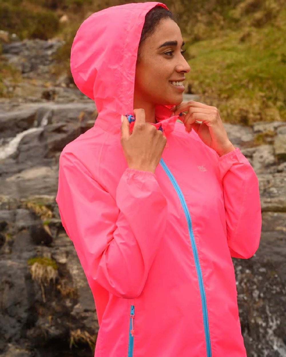 Neon Pink coloured Mac In A Sac Packable Origin Neon Waterproof Jacket on blurry mountain background 