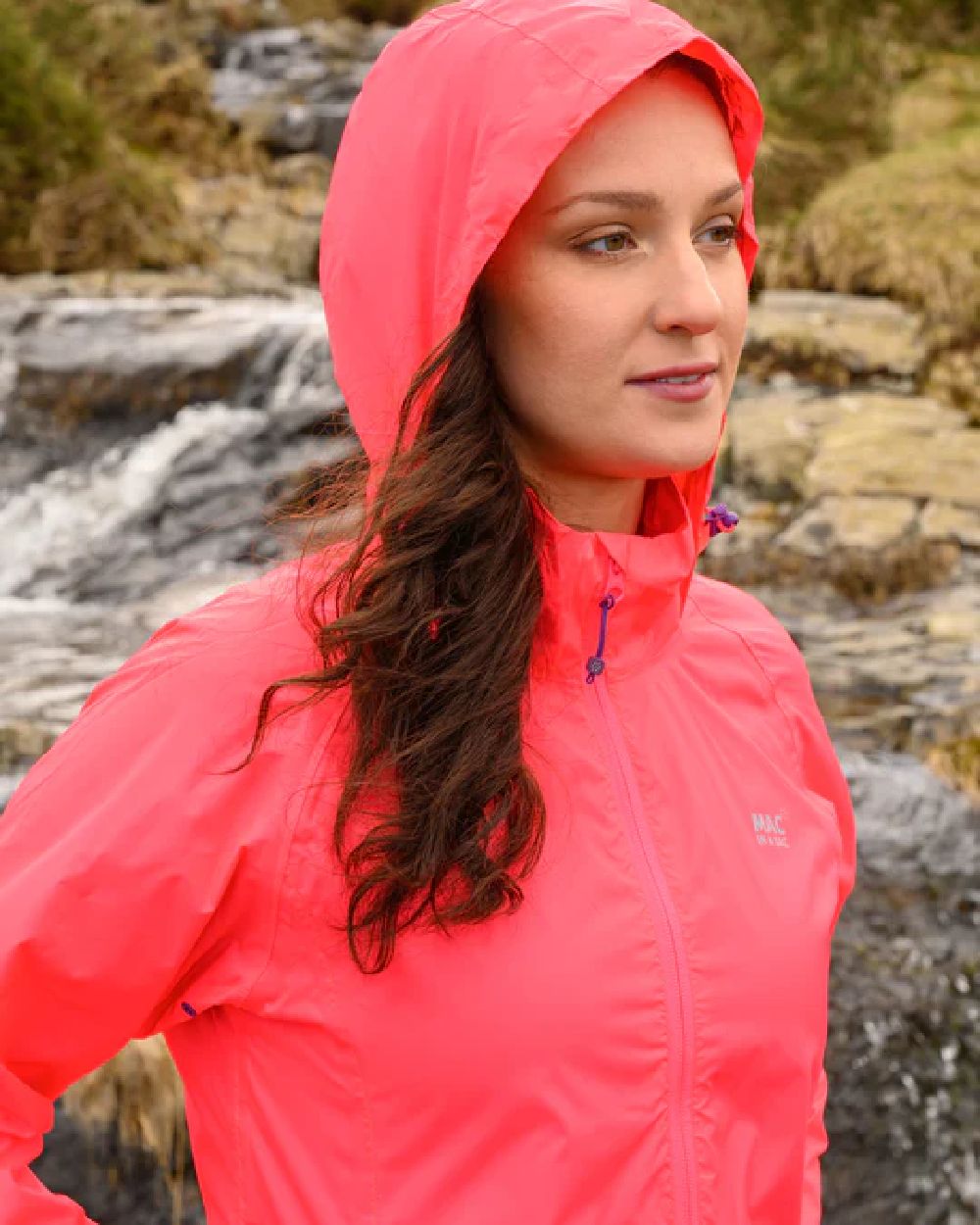 Neon Watermelon coloured Mac In A Sac Packable Origin Neon Waterproof Jacket on blurry mountain background 