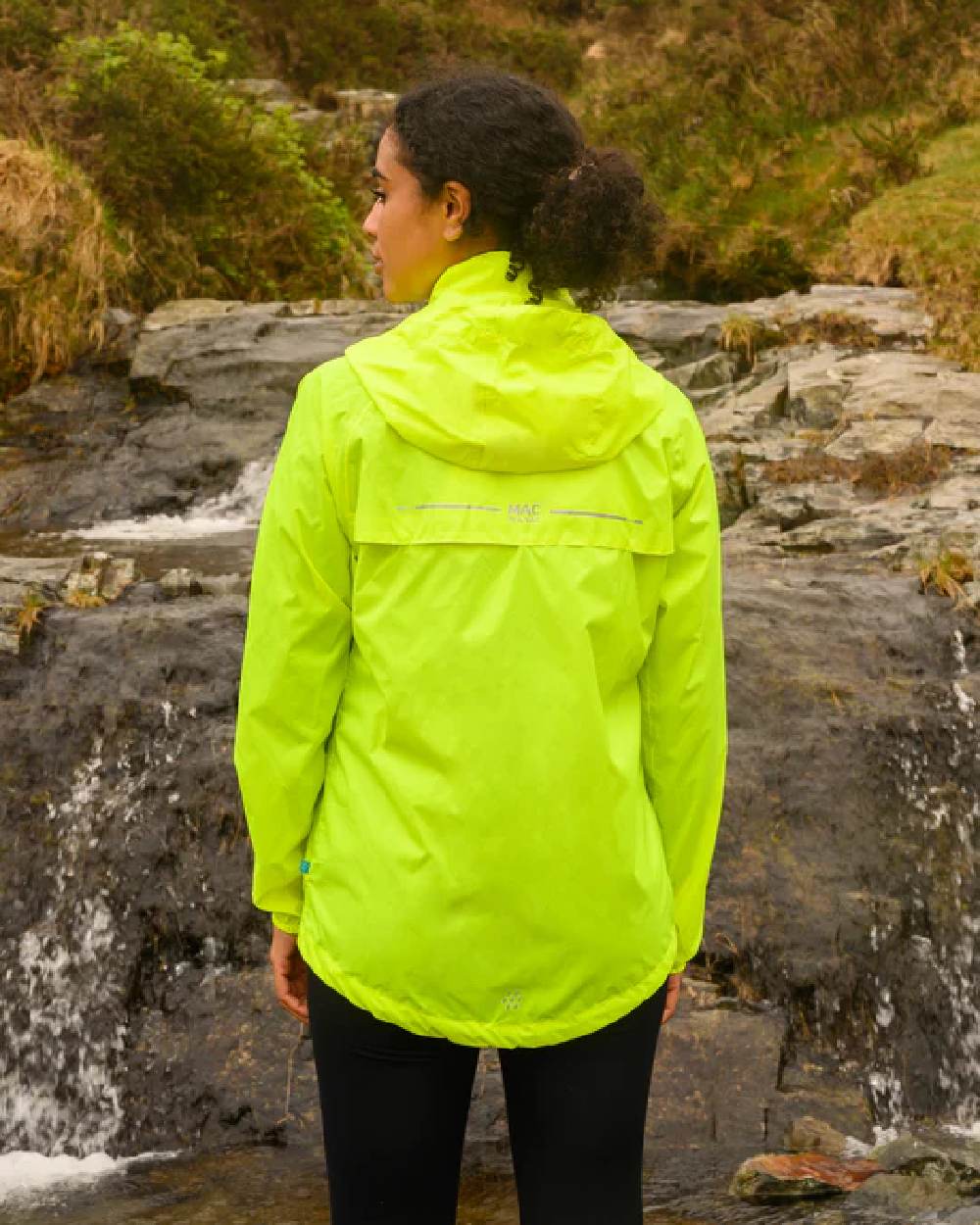 Neon Yellow coloured Mac In A Sac Packable Origin Neon Waterproof Jacket on blurry mountain background 