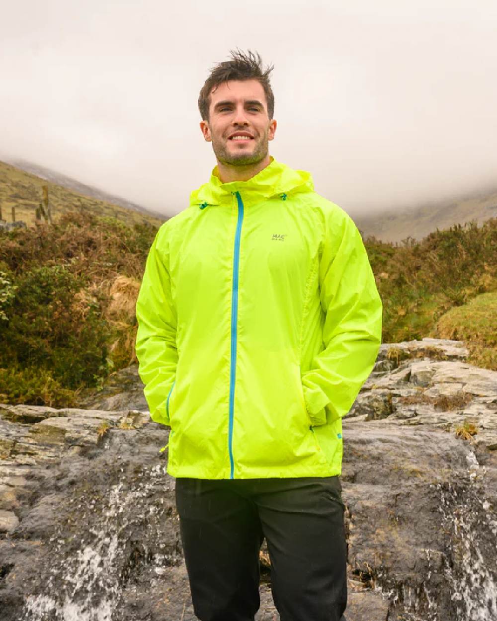 Neon Yellow coloured Mac In A Sac Packable Origin Neon Waterproof Jacket on blurry mountain background 