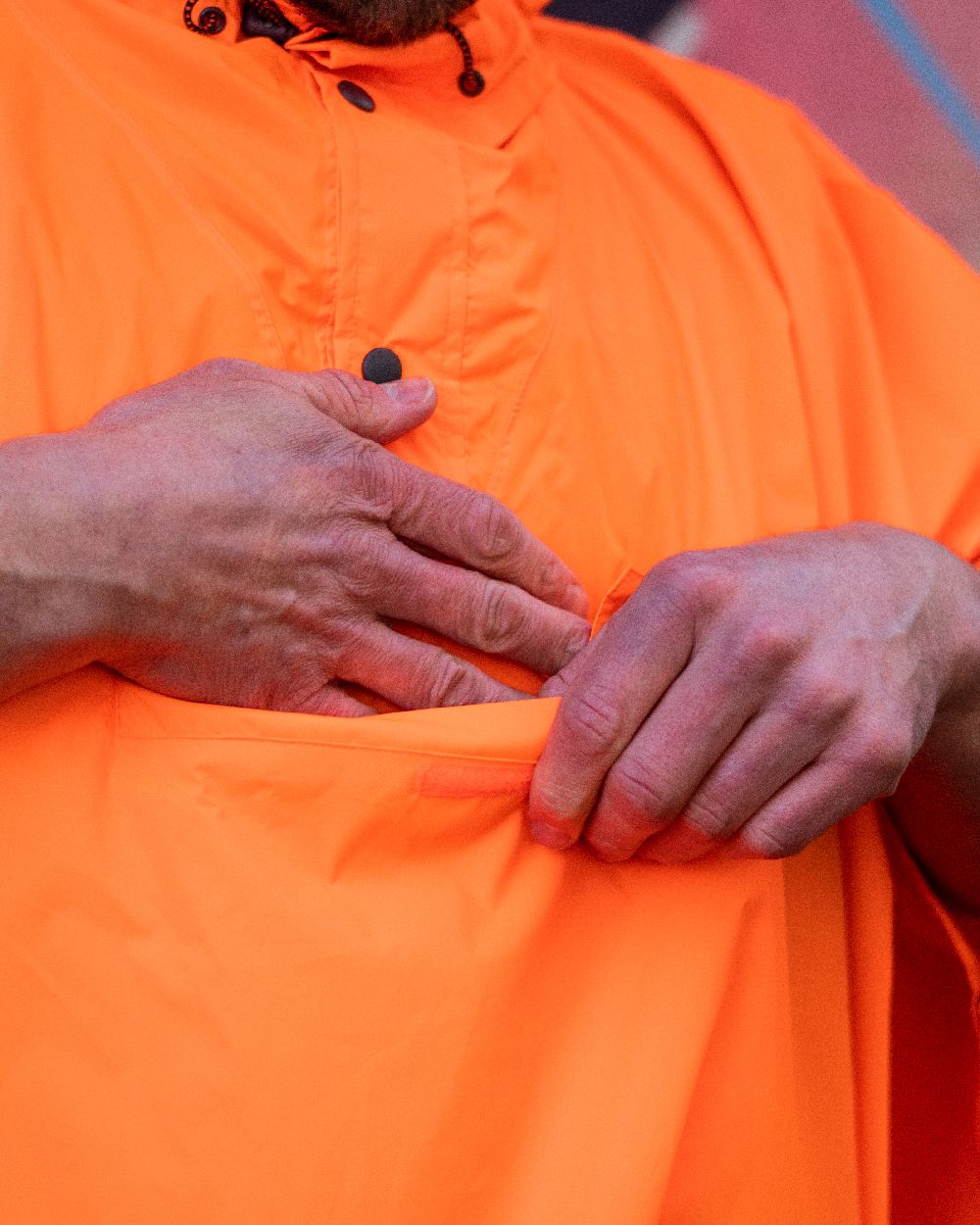 Neon Orange Coloured Mac In A Sac Origin Waterproof Poncho Neon on blurry background 