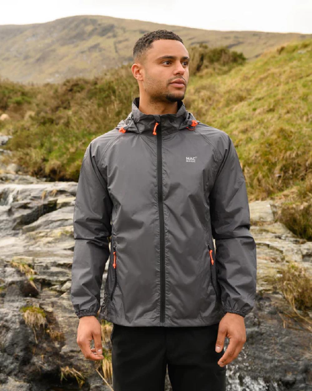 Charcoal coloured Mac In A Sac Packable Origin Waterproof Jacket on blurry mountain background 