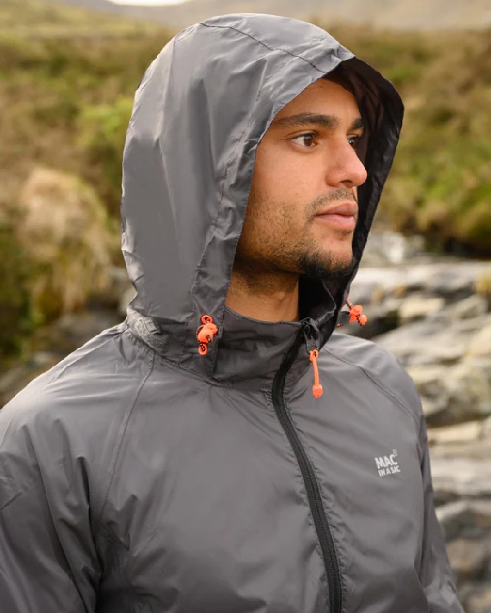 Charcoal coloured Mac In A Sac Packable Origin Waterproof Jacket on blurry mountain background 