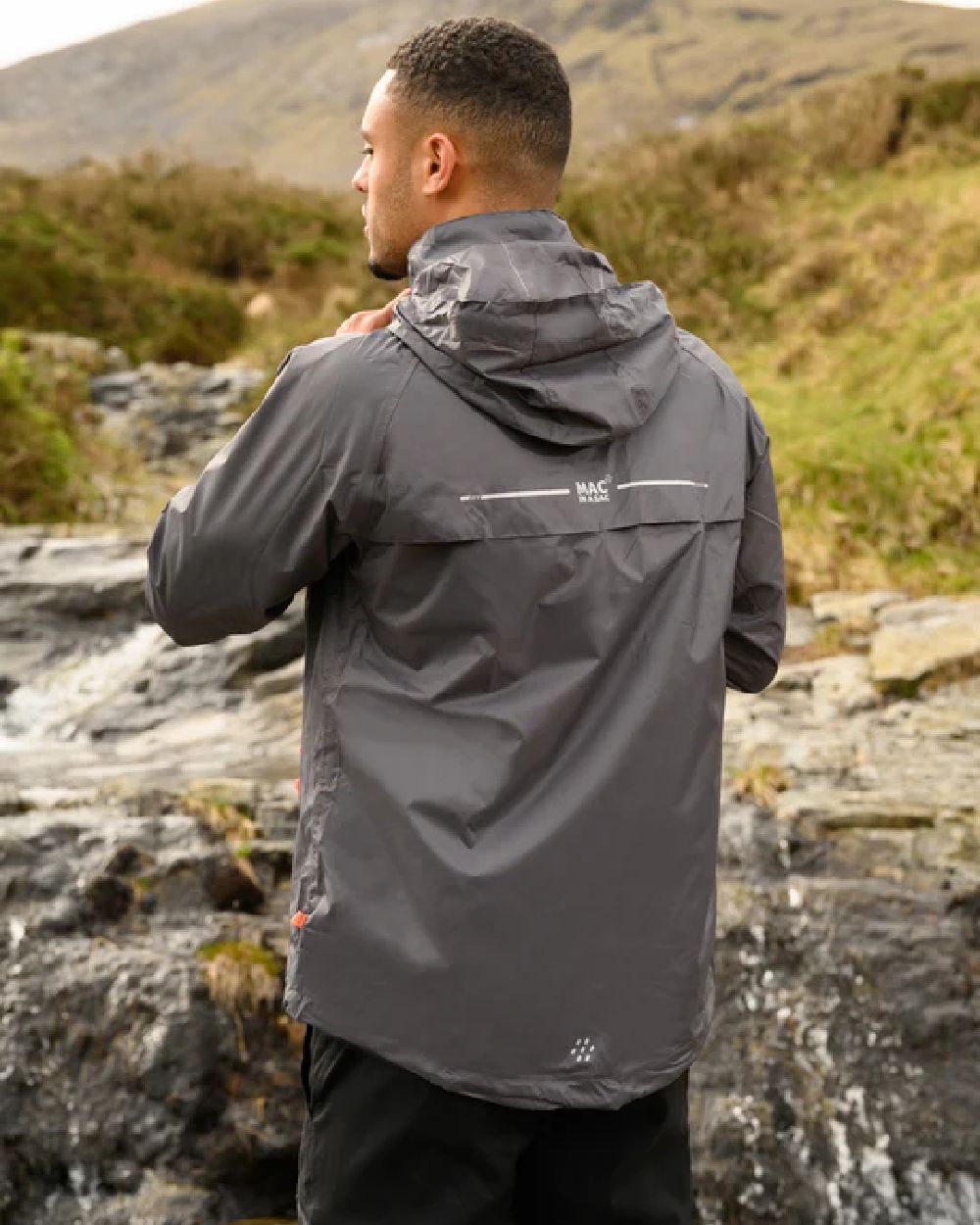 Charcoal coloured Mac In A Sac Packable Origin Waterproof Jacket on blurry mountain background 