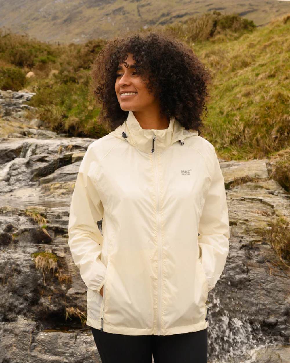 Ivory coloured Mac In A Sac Packable Origin Waterproof Jacket on blurry mountain background 