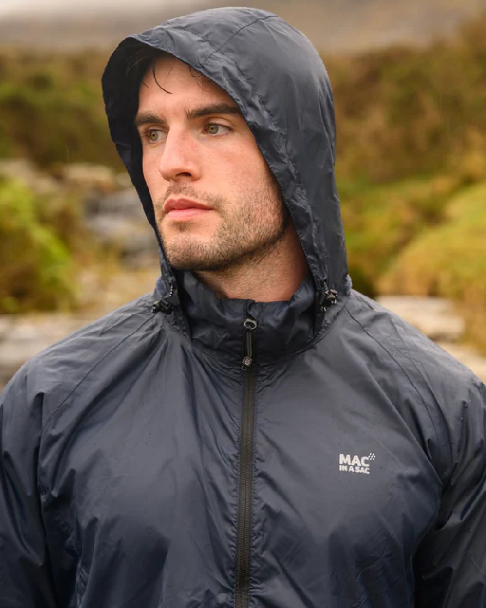 Navy coloured Mac In A Sac Packable Origin Waterproof Jacket on blurry background 