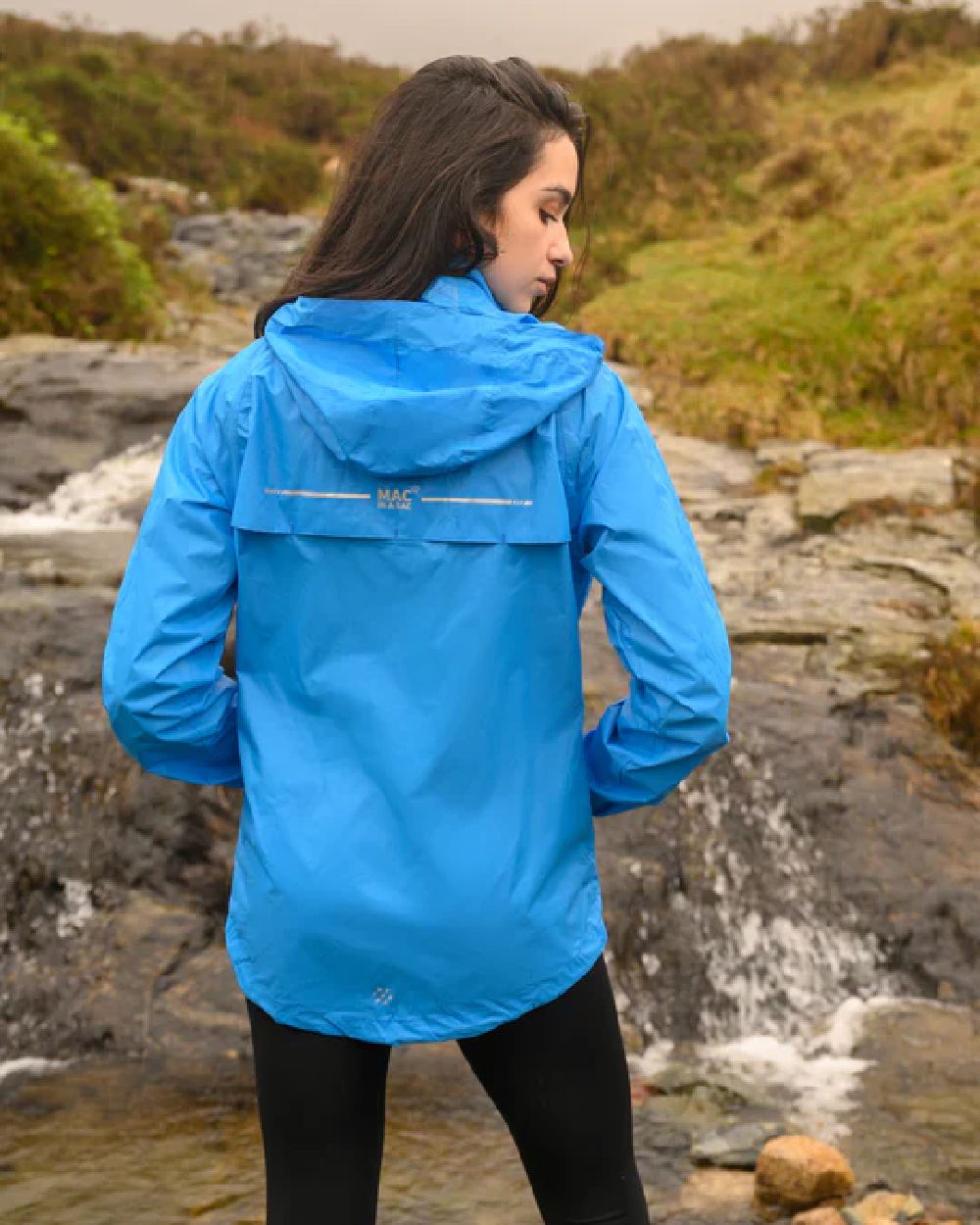 Ocean Blue coloured Mac In A Sac Packable Origin Waterproof Jacket on blurry background 