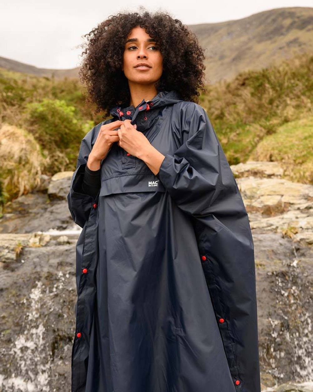 Navy coloured Mac In A Sac Waterproof Poncho on a blurry mountain background 