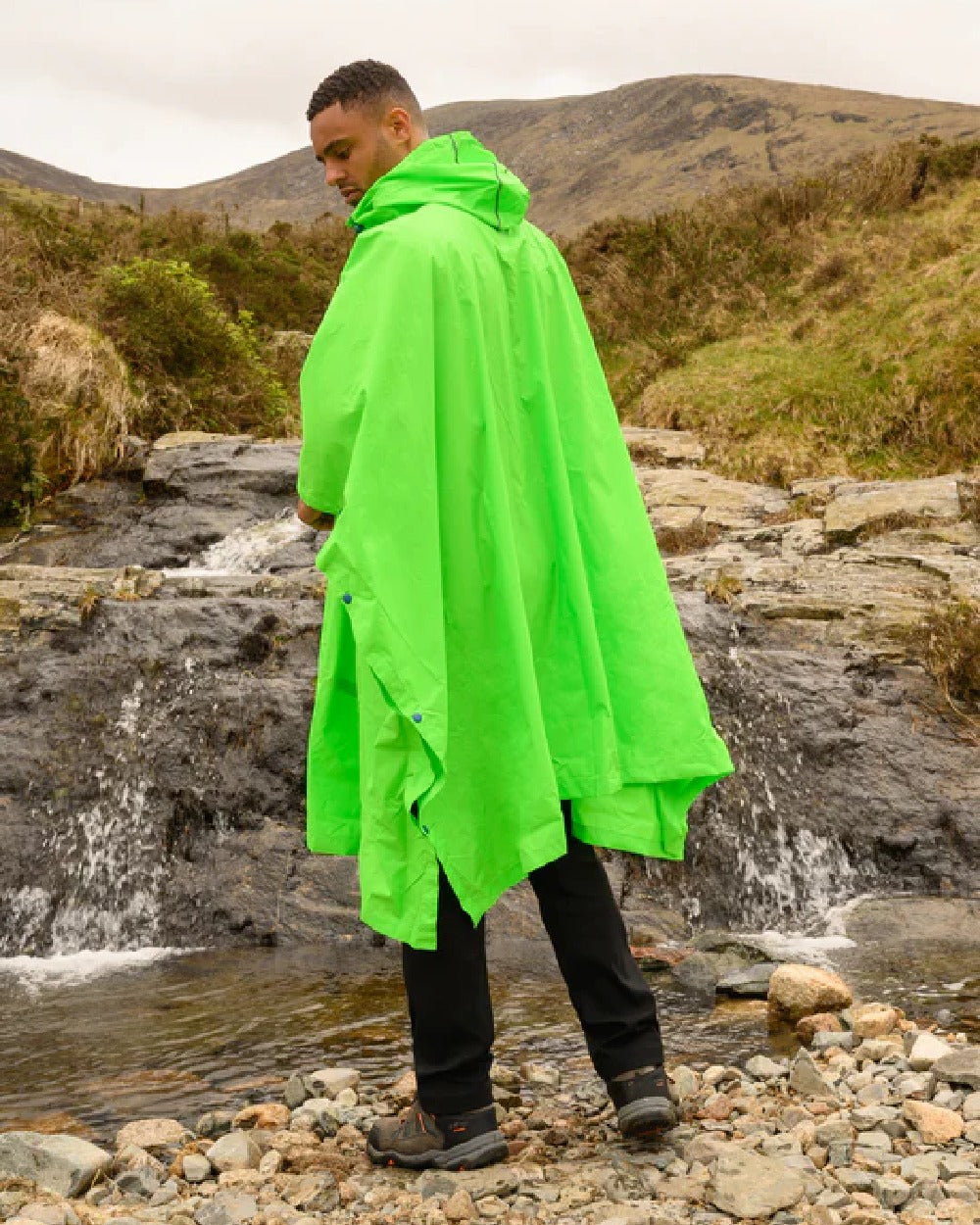 Neon green coloured Mac In A Sac Waterproof Poncho on a mountain background 