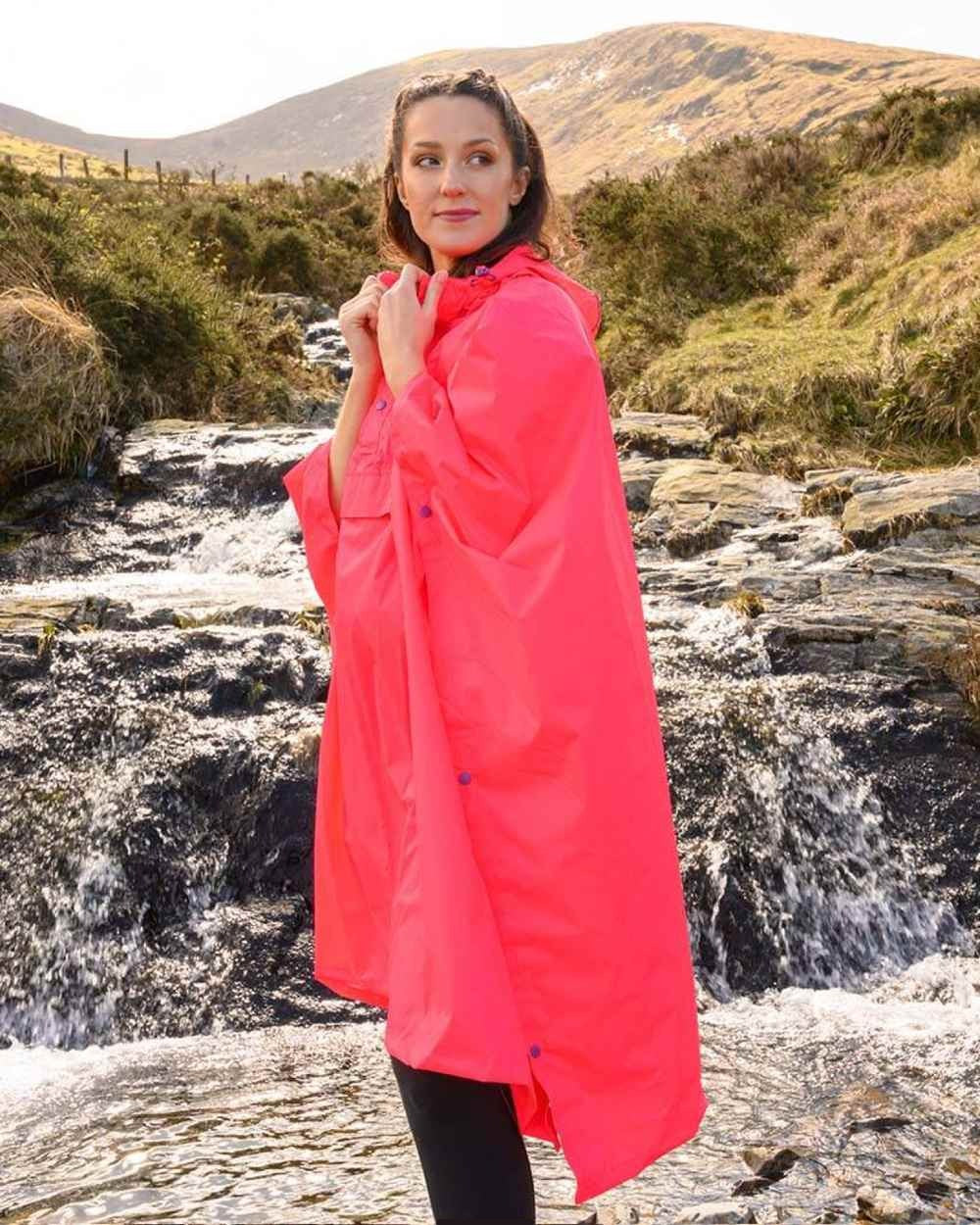 Neon Watermelon coloured Mac In A Sac Waterproof Poncho on a mountain background 