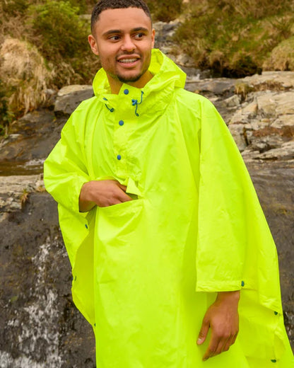 Neon Yellow coloured Mac In A Sac Waterproof Poncho on a blurry mountain background 