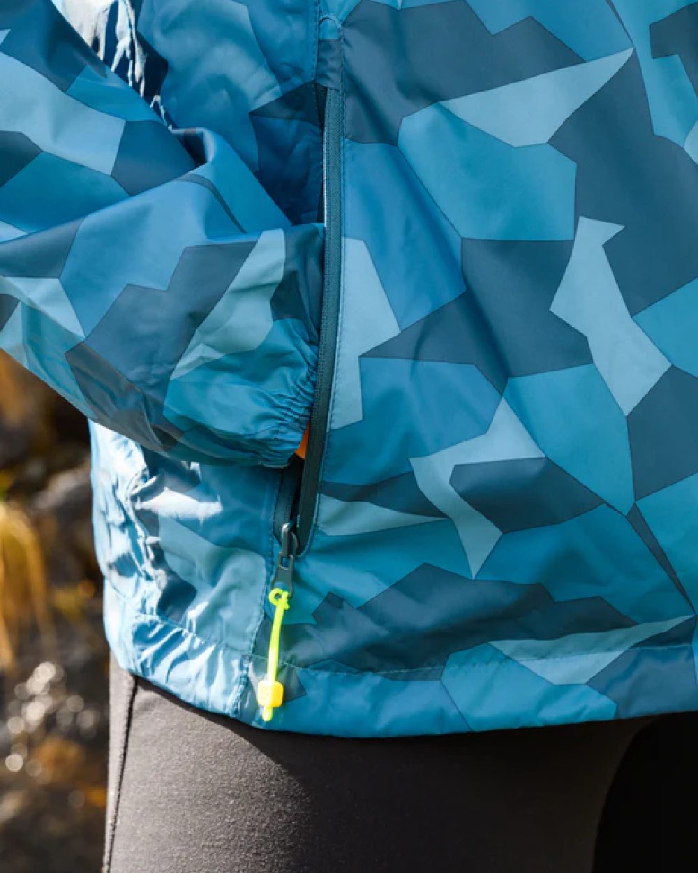 Teal Camo coloured Mac In A Sac Packable Origin Camo Waterproof Jacket on blurry background 