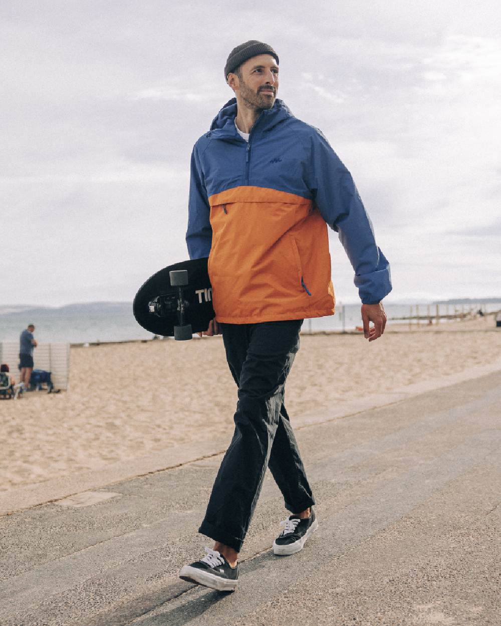 Blue Burnt Orange coloured Mac In A Sac Nomad Waterproof Half Zip Jacket on beach background 