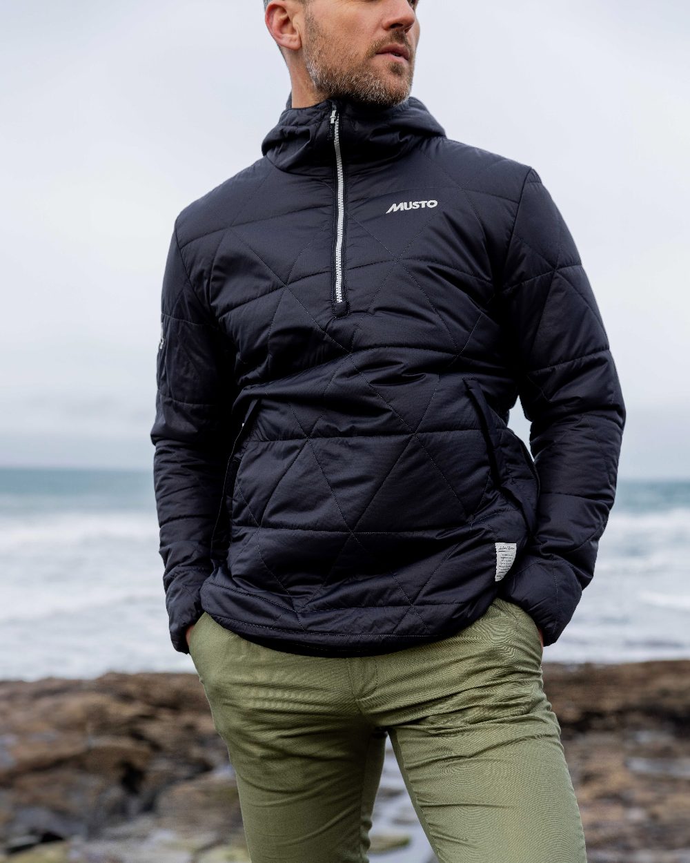 Carbon Coloured Musto Mens 64 Snug Quilt Anorak on sea background 