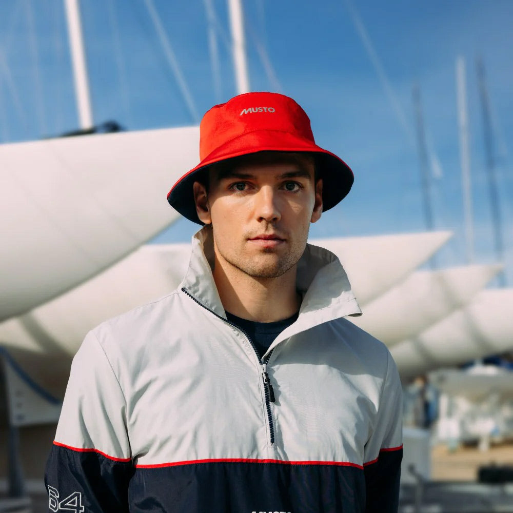 Man in a bright red bucket hat standing in a ship yard.