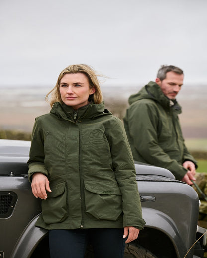 Deep Green Coloured Musto Womens Burnham Waterproof Jacket on Landscape with Vehicle Background 
