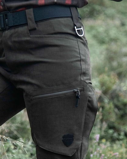 Dark Green coloured Northern Hunting Womens Alva Una G2 Hunting Trousers on forest background 