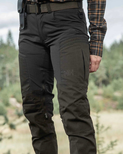 Dark Green coloured Northern Hunting Womens Tyra Pro Outdoor Trousers on forest background 