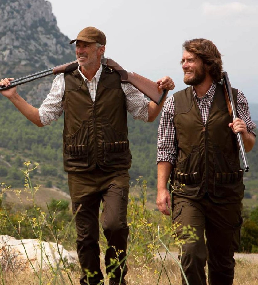 Two men carrying shotguns while walking through countryside terrain during a rough shoot