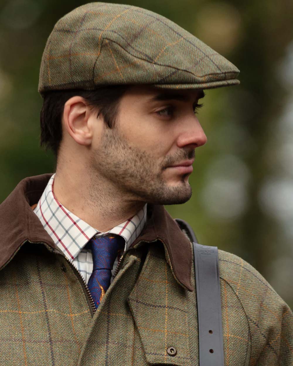 Dark Moss coloured Alan Paine Rutland Waterproof Tweed Shooting Coat on forest background 
