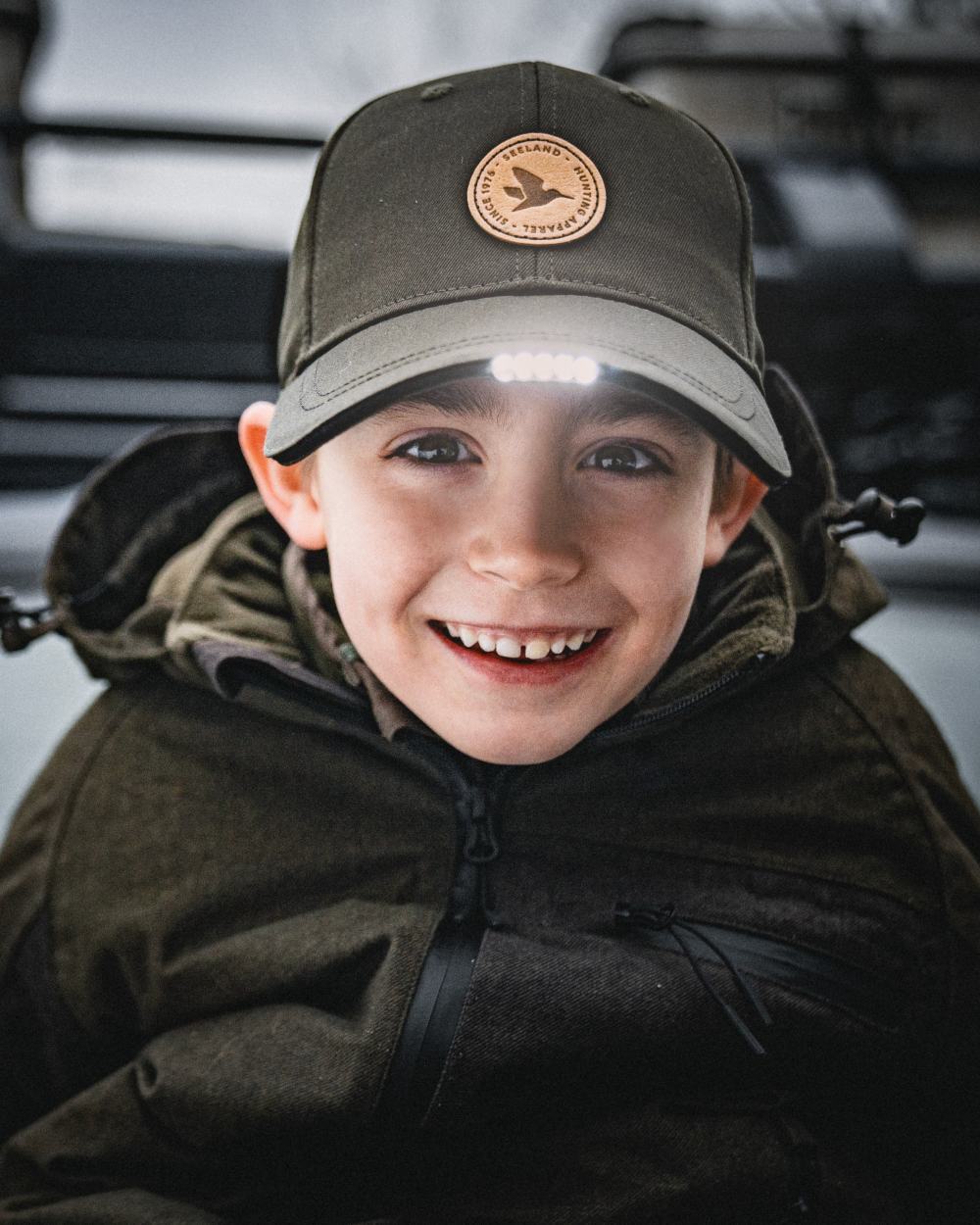 Pine Green coloured Seeland Childrens Skarn LED Junior Cap on forest background 