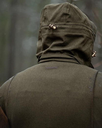 Shaded Olive coloured Seeland Mens Woodcock Royale Jacket on forest background 