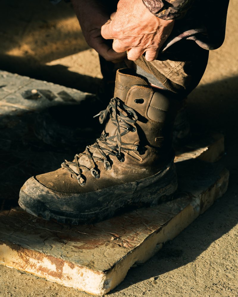 Person tightening shooting boot laces outdoors while preparing for countryside activity