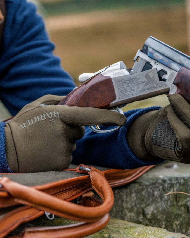 Person wearing Härkila shooting gloves while handling a shotgun outdoors