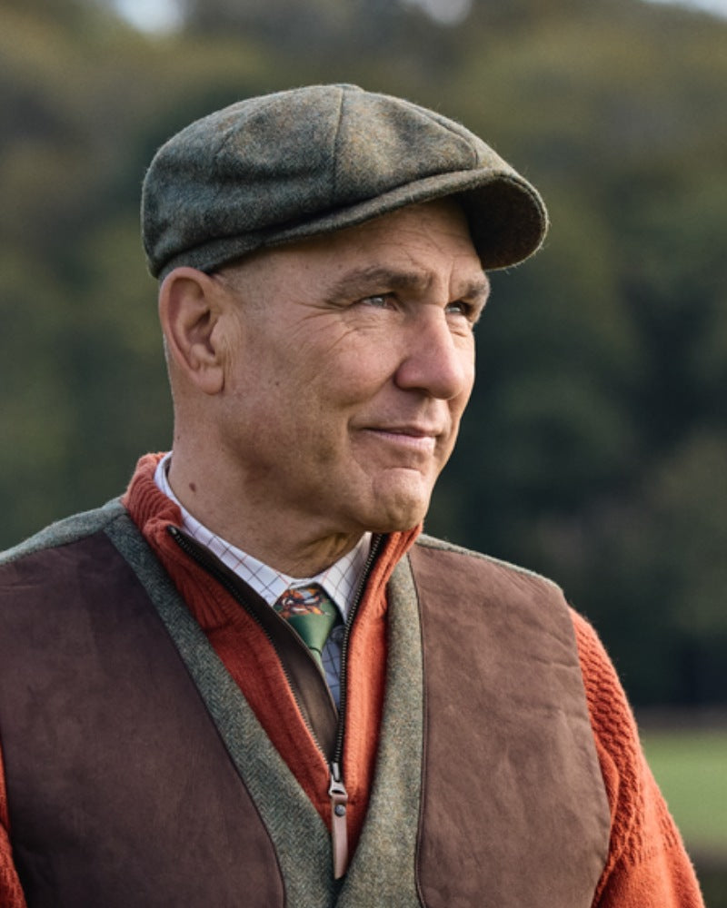 Man wearing a Härkila tweed flat cap with traditional country clothing outdoors