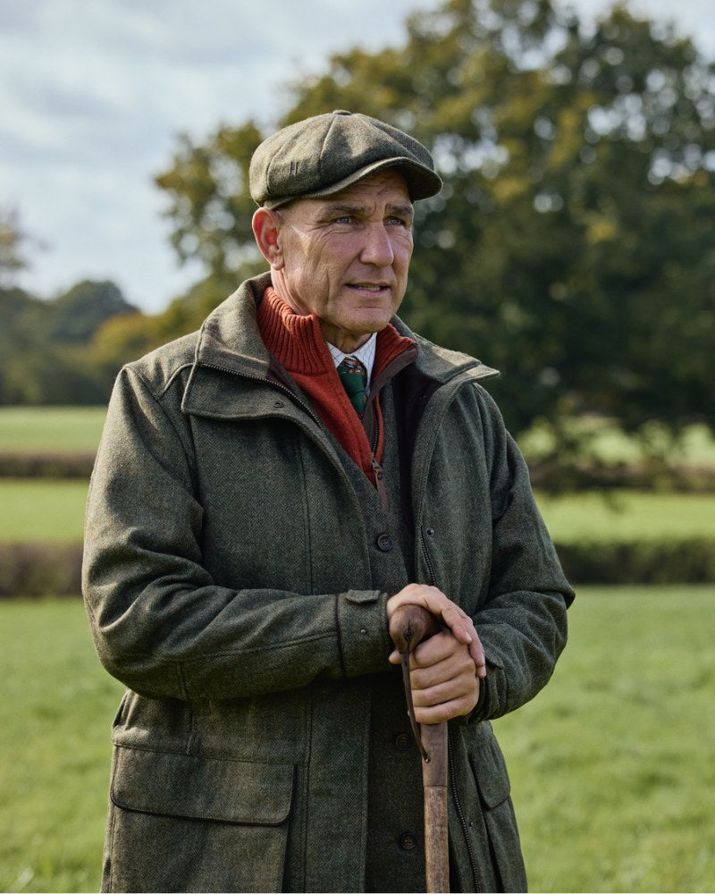 Man wearing a Härkila country jacket and flat cap outdoors in a rural setting