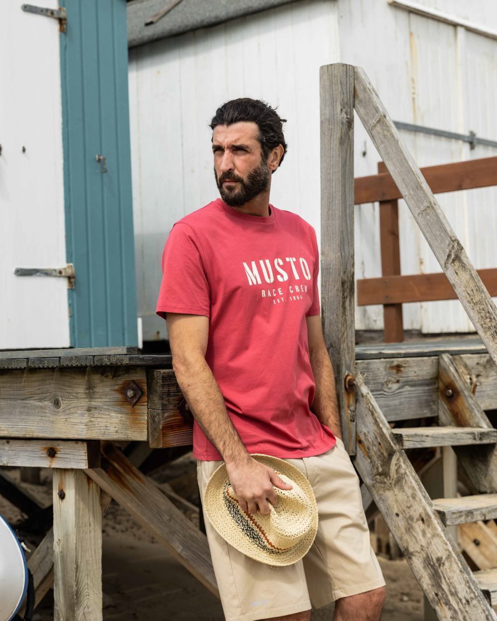 Sweet Raspberry Coloured Musto Mens Classic Short Sleeve T-Shirt On A Coastal Background 