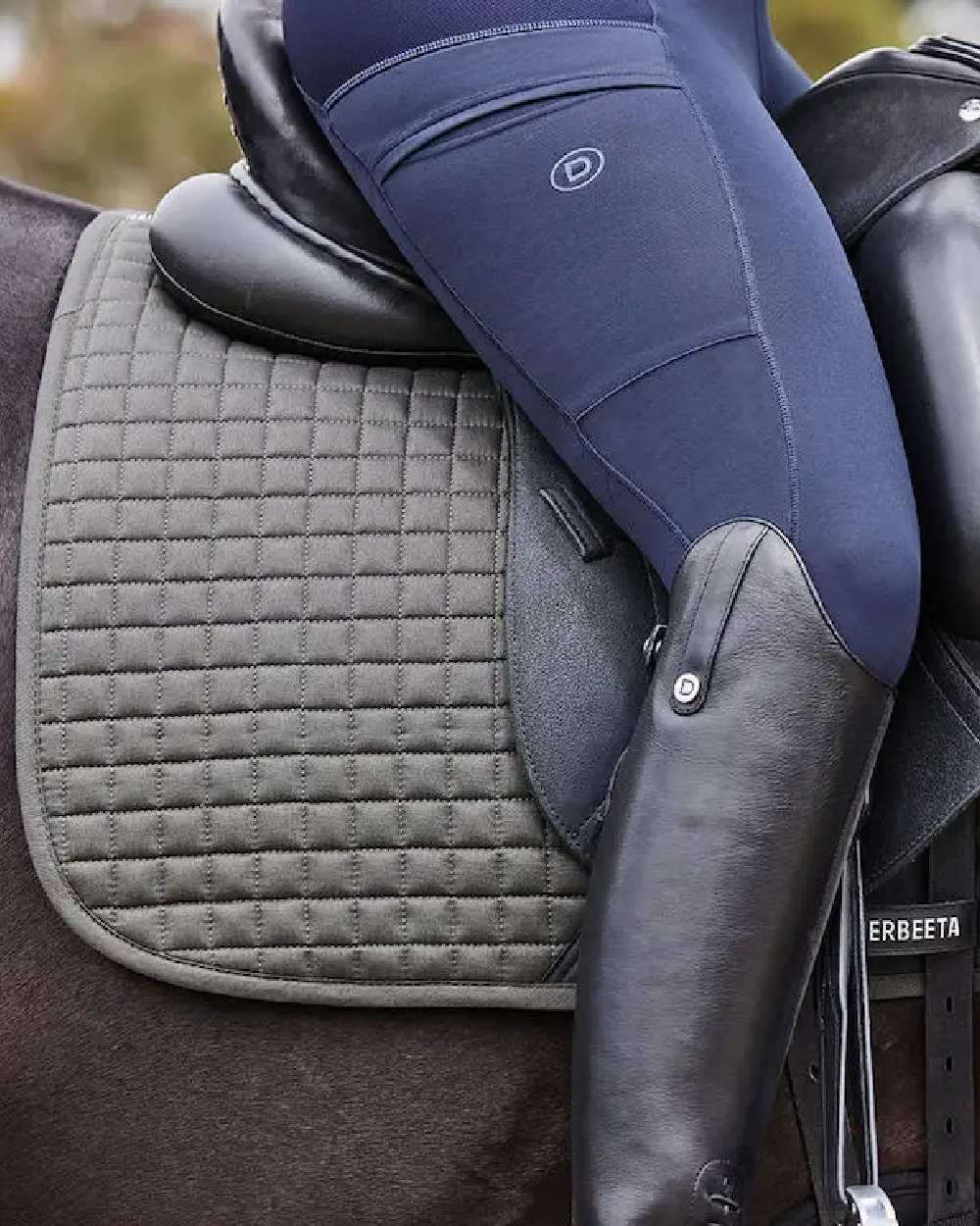 Olive coloured WeatherBeeta Prime Dressage Saddle Pad on blurry background 