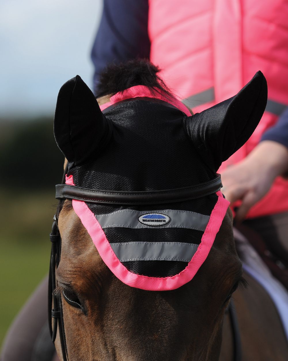 Pink coloured WeatherBeeta Reflective Ear Bonnet on field background 