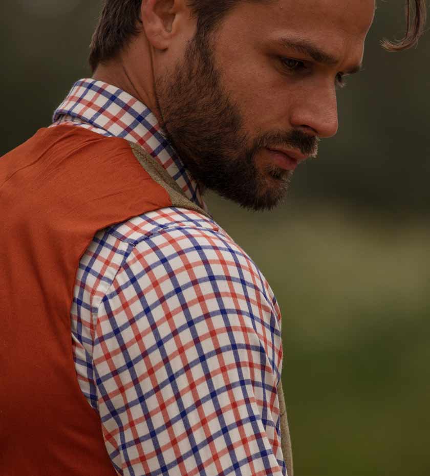 Sleeve of alan Paine Tattersall shirt with red and blue checks, with man's face and blurred background.