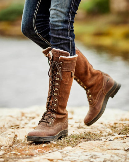 Dark Brown Coloured Ariat Wythburn Tall Waterproof Boots On A Countryside Background 