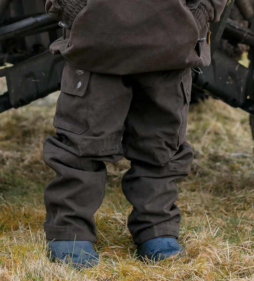 Small child wears cargo trousers in dark green standing on grass.