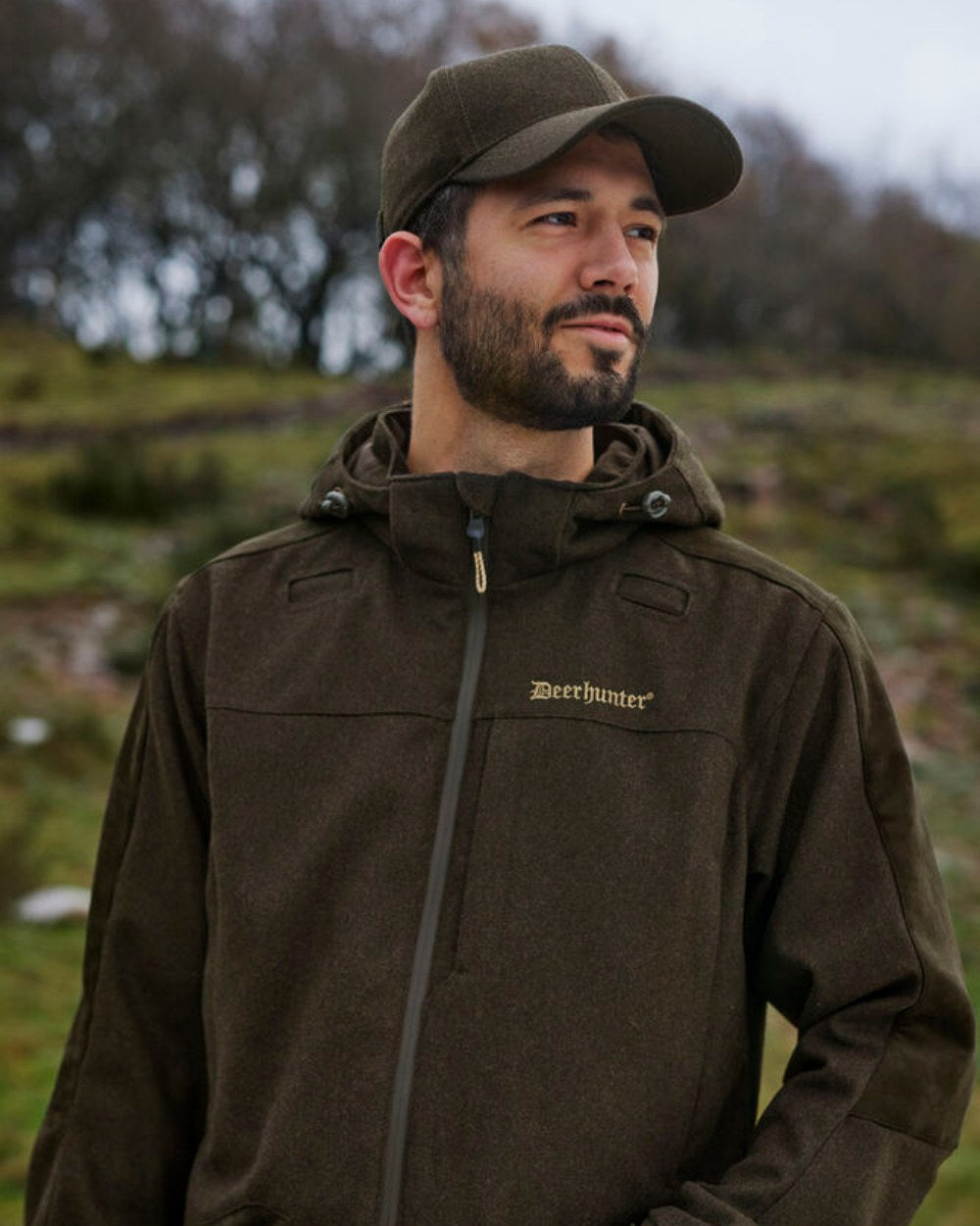 Loden Wood Coloured Deerhunter Tatra Cap With Earflaps On A Forest Background 