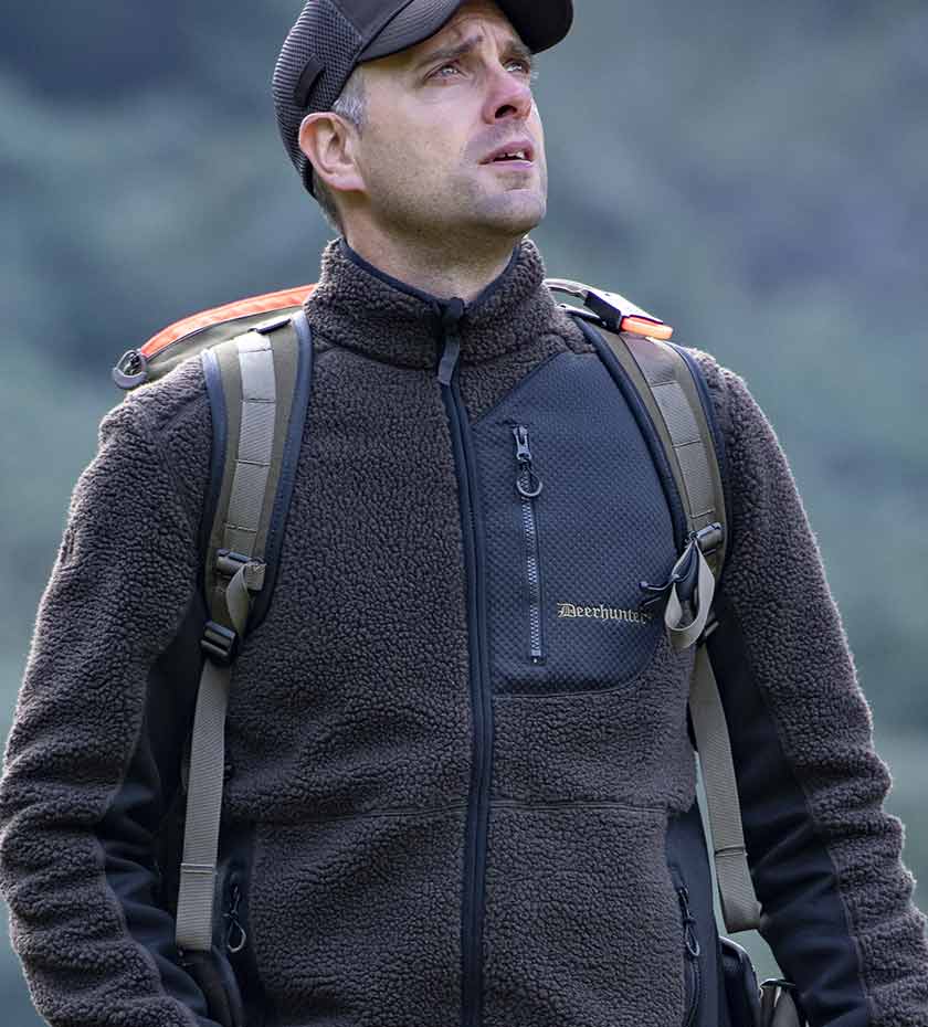 Man wears Deerhunter hunting fleece in dark green with rucksack and shooting cap.